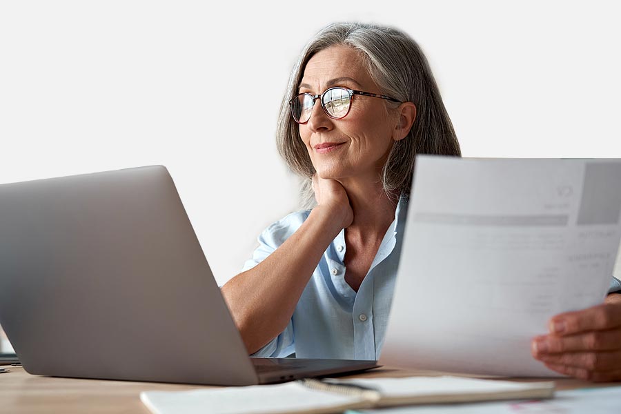 An woman wearing glasses smiling while sitting in front of a laptop