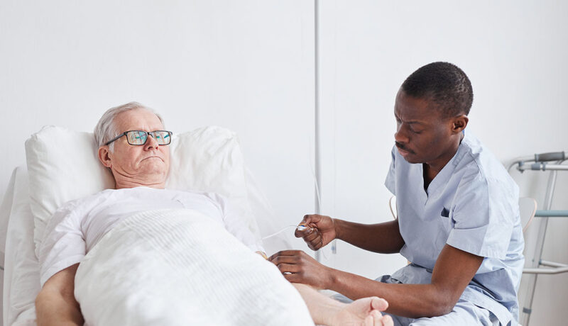 An African American Man Preparing IV Therapy for a Senior Man Laying on a Bed Benefits of Senior IV Therapy